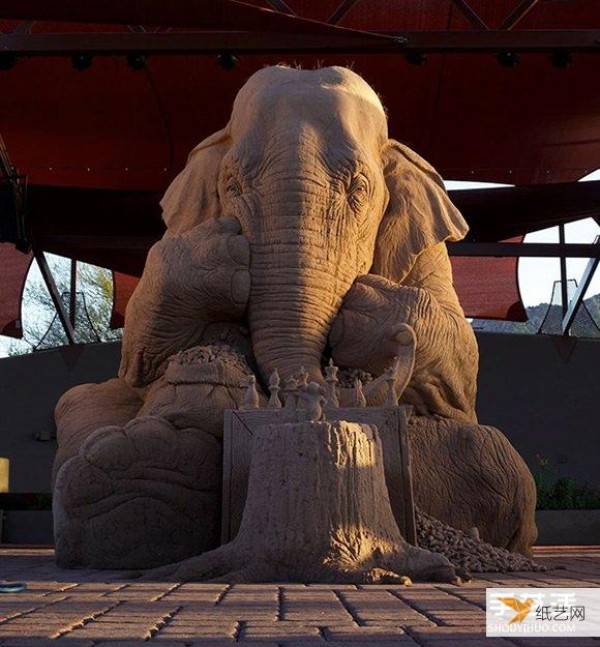 A sand sculpture in the shape of an elephant and mouse playing chess that looks lifelike and full of fairy tale atmosphere