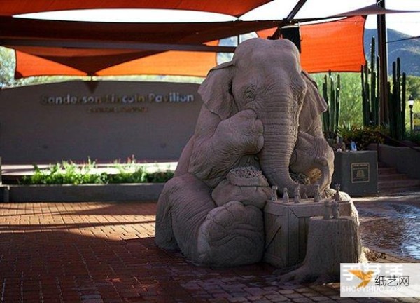 A sand sculpture in the shape of an elephant and mouse playing chess that looks lifelike and full of fairy tale atmosphere