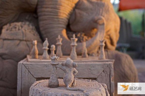 A sand sculpture in the shape of an elephant and mouse playing chess that looks lifelike and full of fairy tale atmosphere